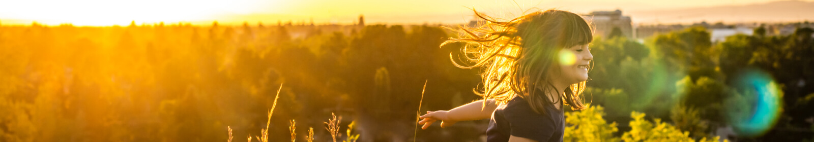 Girl running through a field at sunset.